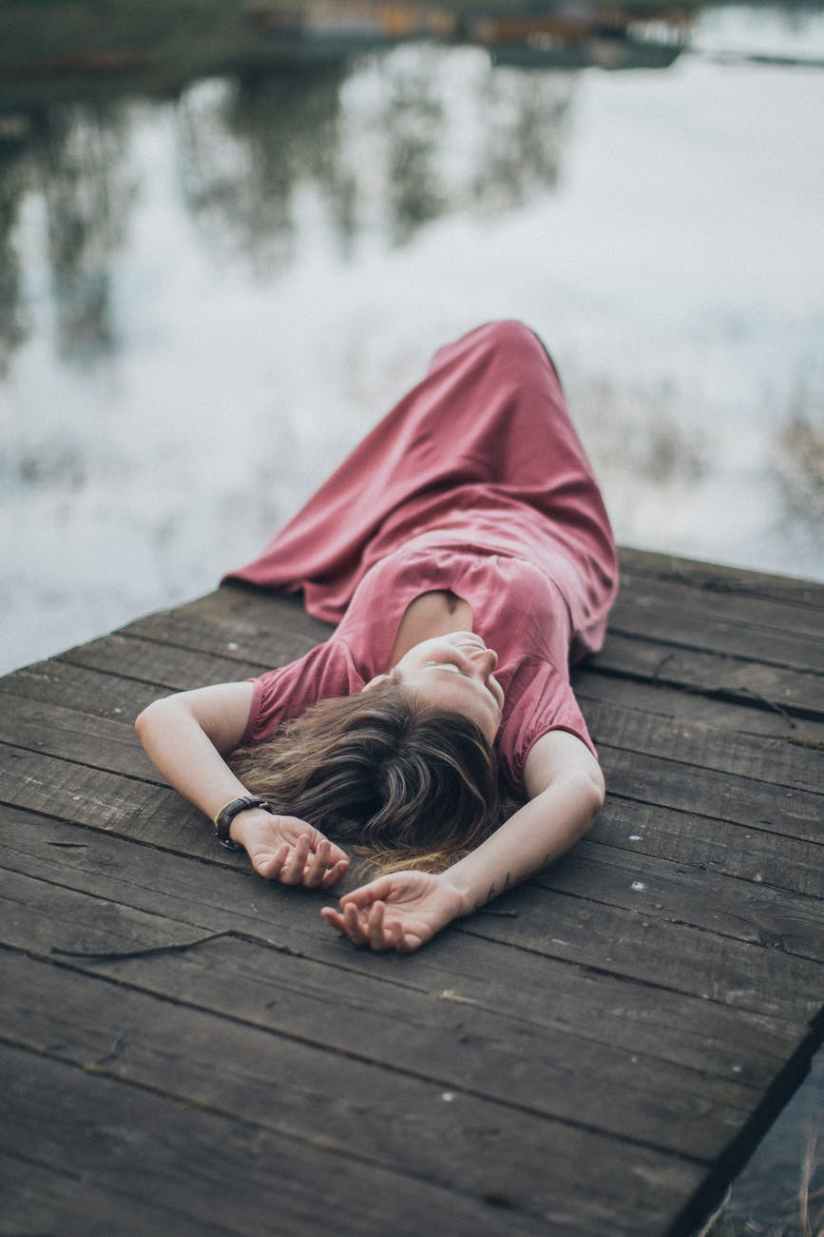 woman in pink dress lying on brown wooden dock